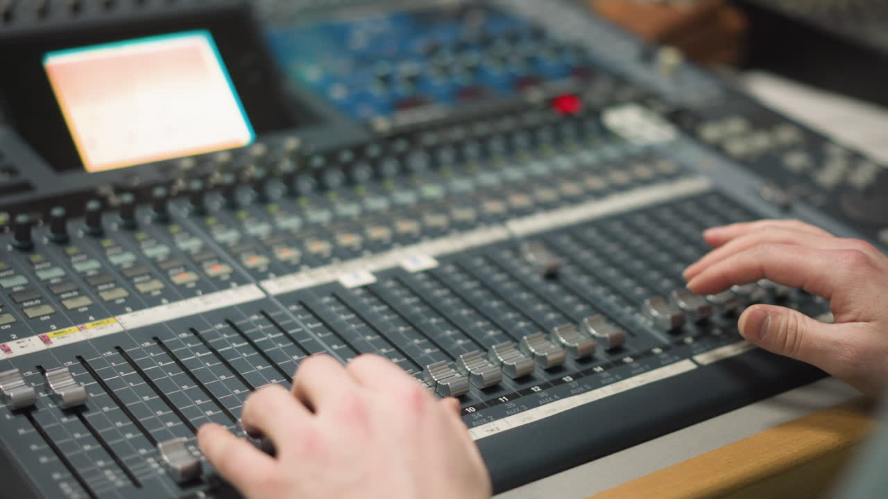 Close-up of hands adjusting audio faders on a professional mixing console. Sound engineer controls multiple audio levels for live broadcast, radio, or music recording with focus on precise adjustments