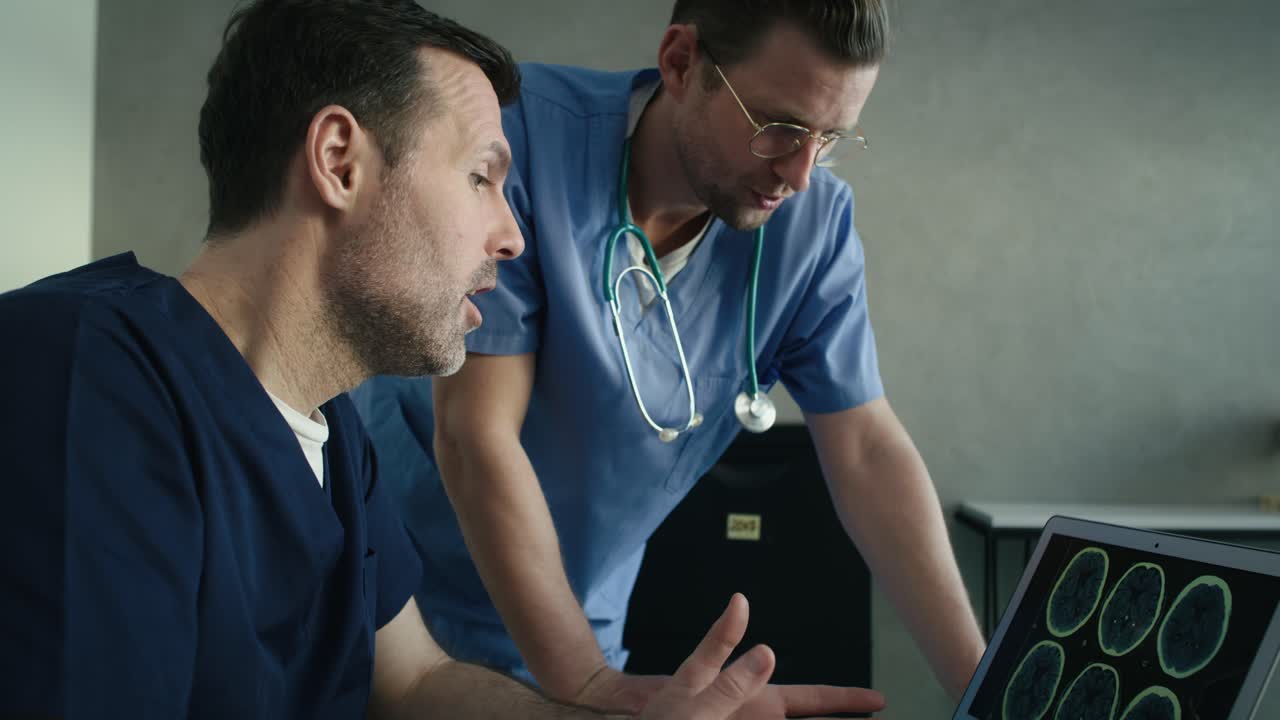 Vista laterale di due medici caucasici maschi che discutono una radiografia medica su un laptop.