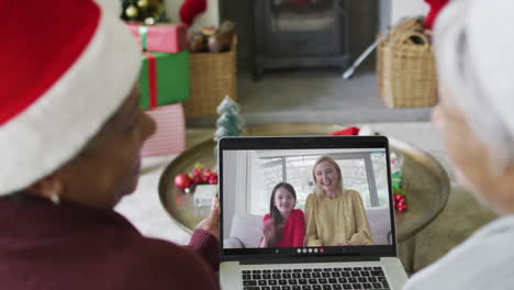 diversas amigas mayores que usan una computadora portátil para una videollamada de navidad con una familia feliz en la pantalla