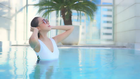 Después-De-Peinarse-El-Pelo-Mojado,-Una-Mujer-Joven-En-La-Piscina-De-Un-Centro-Turístico-Levanta-La-Cara-Hacia-La-Luz