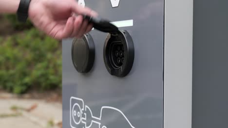 disconnecting electric car cable from outdoor charging station, hand close up