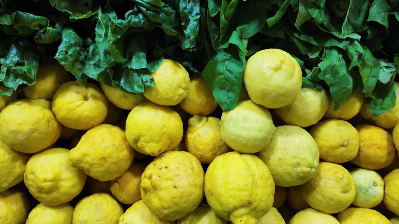 Tilt-down shot of fresh lemons, limes, and Swiss chard, showcasing vibrant colors, natural textures, and fresh produce in a market