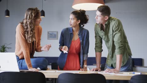 diverse male and female colleagues in discussion using laptop and notes in casual office meeting