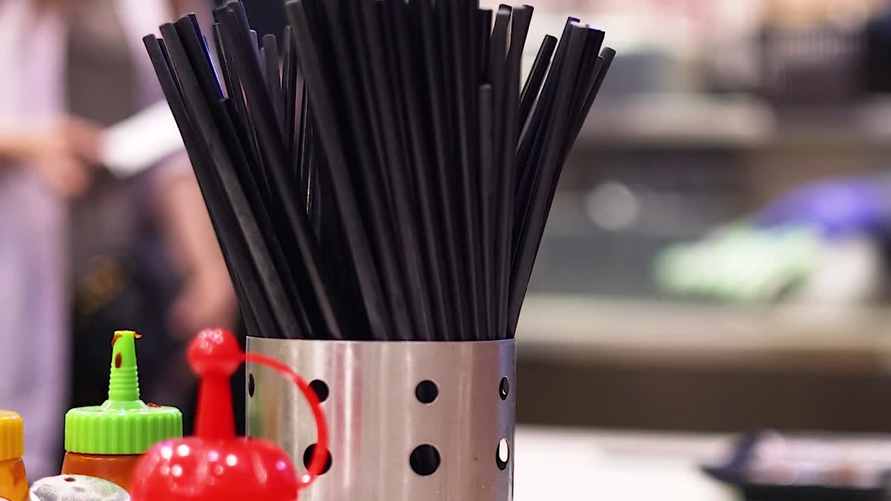 Close-up of chopsticks and condiment bottles on a bustling restaurant counter.
