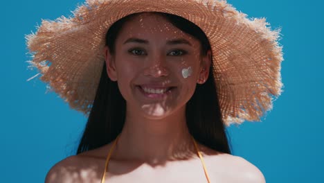 young asian woman puts some sunscreen on her cheek and smiles