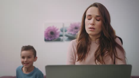 Tired-mother-working-on-laptop-at-home.-Boy-interrupt-busy-mom