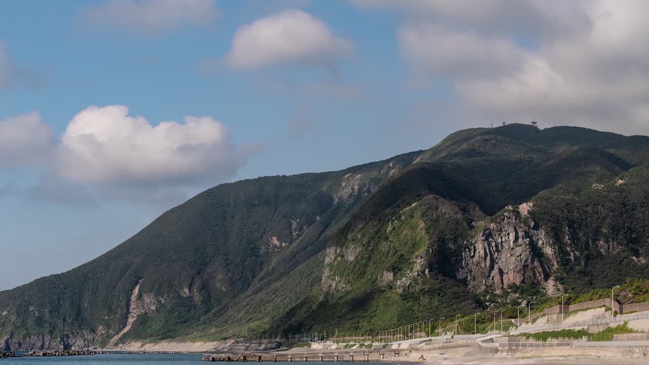 Timelapse di nuvole in rapido movimento che proiettano ombre su scogliere verdi con oceano e spiaggia in primo piano - Panoramica