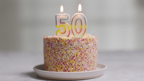 studio shot birthday cake covered with decorations and candle celebrating fiftieth birthday being blown out