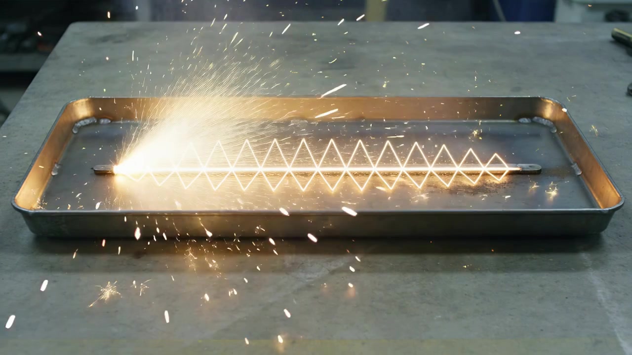 Elemento a zigzag luminoso che invia scintille da una barra di metallo attraverso un banco, riempiendo un vassoio di frammenti