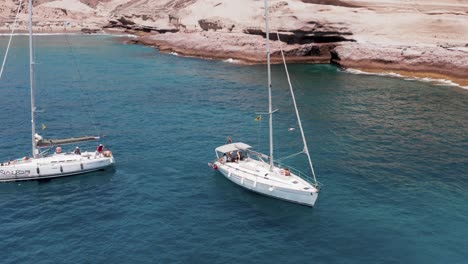 Two-sailing-yachts-anchored-near-rocky-shore-of-Tenerife-island,-aerial