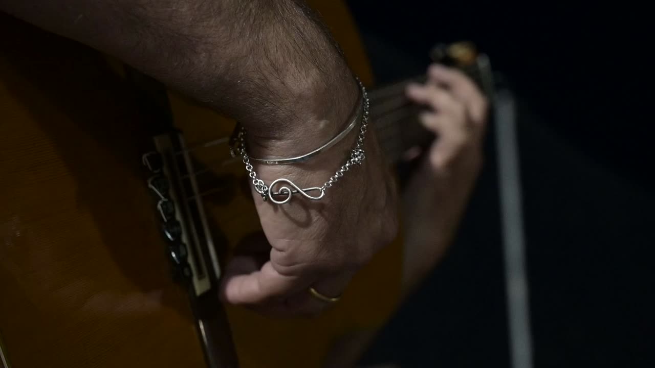 primer plano de un guitarrista tocando una guitarra clásica con un brazalete de clave aguda en su muñeca