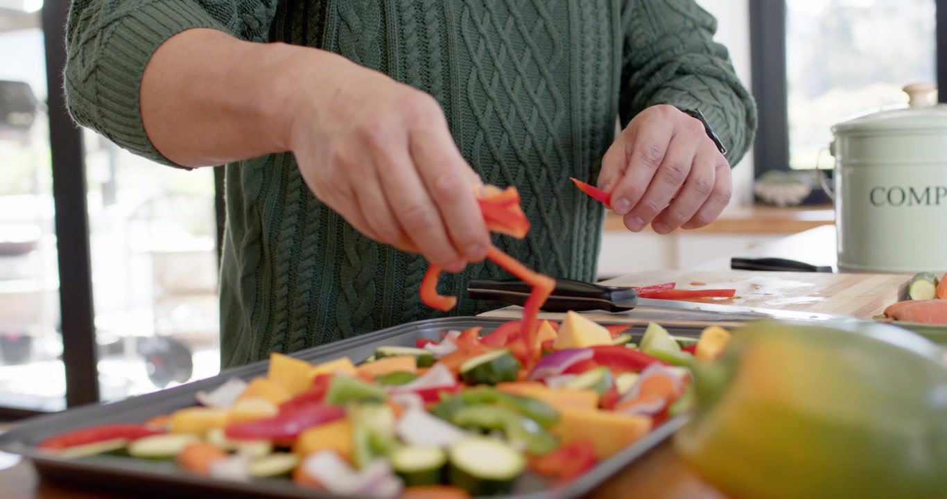 Cook is trimming red bell pepper, arranging strips on sheet pan on wooden counter for roasting