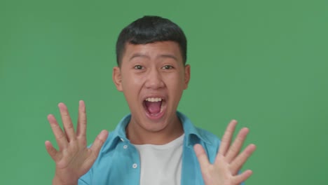 the shocked young asian boy grabbing his head while saying wow on green screen background in the studio
