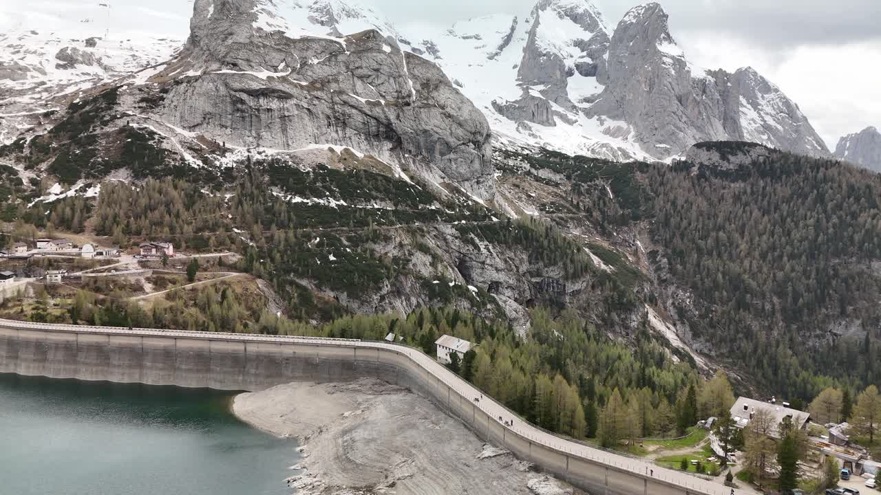 Aerial drone flight over Lago di Fedaia turn up to dramatic peaks of Marmolada in the Dolomites, Italy. Moody overcast light enhances the alpine textures and rugged mountain landscape