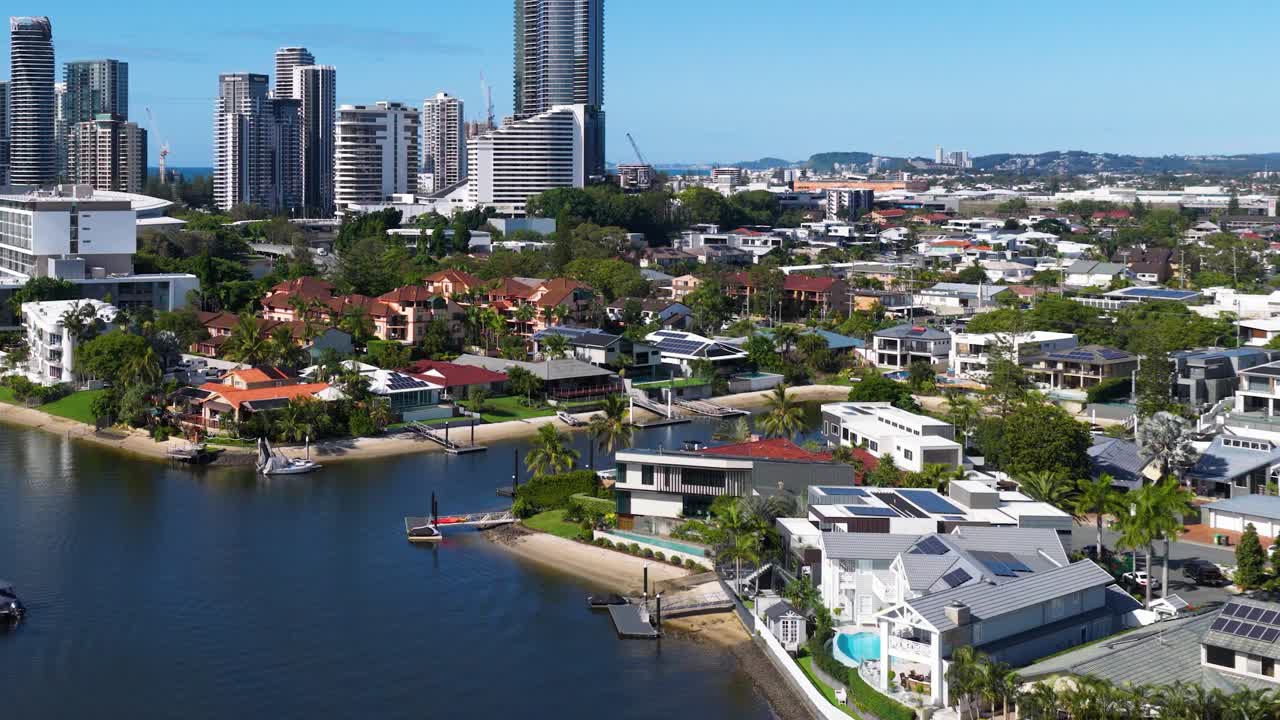 Aerial footage captures the Gold Coast's waterfront homes and skyline under bright daylight, showcasing urban and natural beauty