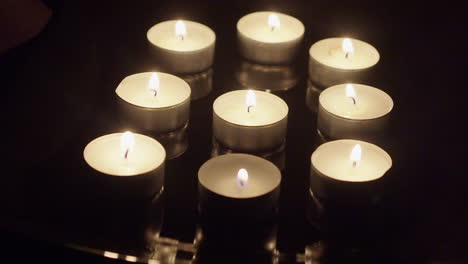 nueve velas de té queman llamas en la superficie reflectante en una habitación oscura