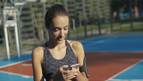 sporty girl with airpods laughing while texting message on smartphone at outdoor court on a summer day 1