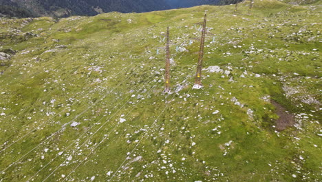 Aerial-View-Of-High-Voltage-Towers-And-Cables-In-The-Middle-Of-Green-Fields-And-Rocks-In-The-Alps,-Passo-San-Marco,-Northern-Italy---aerial-drone-shot