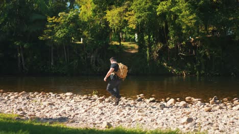 young male hiker in walks in slow motion along rocky river hot summer day, outdoor activity and travel in nature