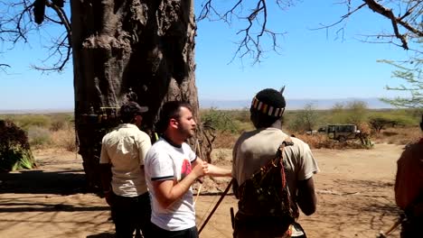 Unrecognizable-Hadzabe-tribe-people-teach-white-tourist-man-how-to-use-a-bow