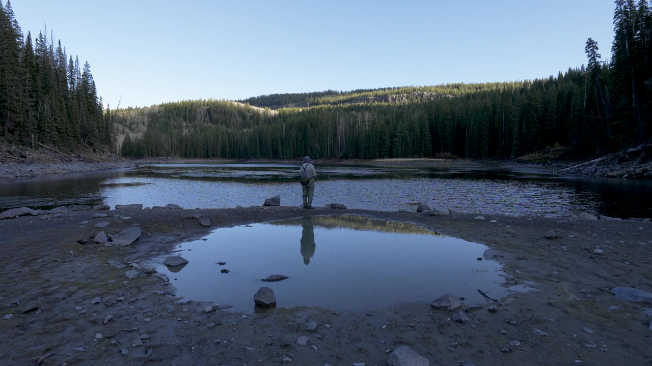 Stille vidvinkelopptak fra bakken av en enslig fisker som kaster snøret ved en stille alpesjø på Colorados Grand Mesa, og fisker etter regnbueørret og bekkerøye i Rocky Mountains