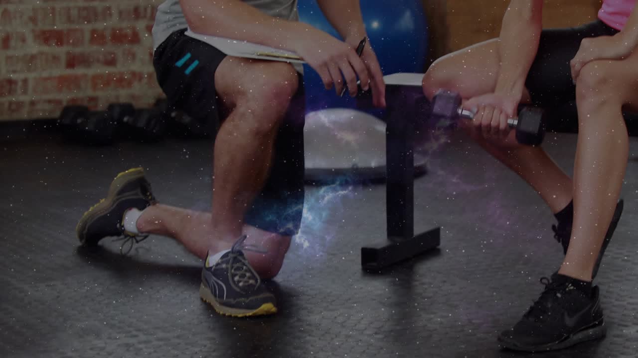 Trainer kneeling and cueing client doing bicep curls on gym bench noting form to improve