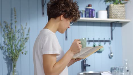mujer bebiendo café y leyendo un libro en la cocina