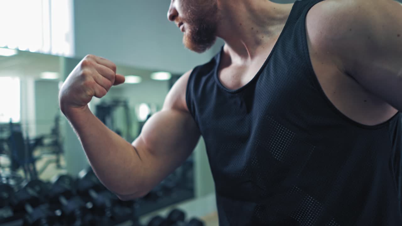 Close-up muscles on man's arm in sports club. Strong bodybuilder in sportswear showing his biceps in fitness center.