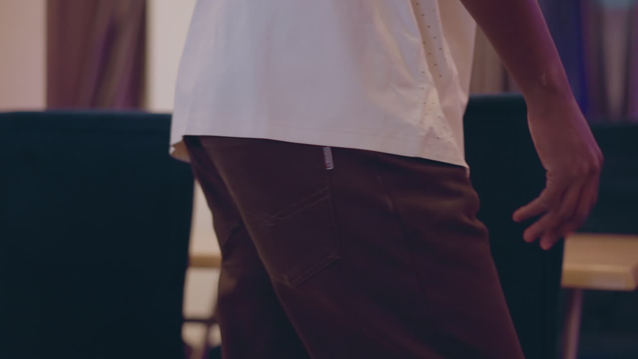 Close-up of person in white shirt with hand on backrest of blue chair, setting up furniture in modern room, arranging chairs on wooden floor, preparing space for meeting or event