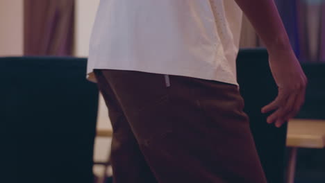 close-up of person in white shirt with hand on backrest of blue chair, setting up furniture in modern room, arranging chairs on wooden floor, preparing space for meeting or event