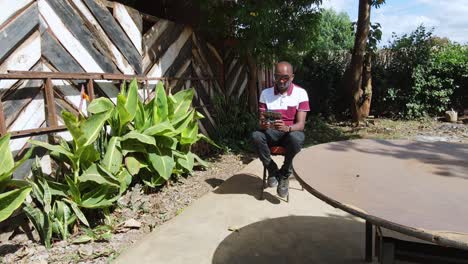 Porträt-Eines-Afrikanischen-Mannes,-Der-Im-Garten-Sitzt-Und-Eine-Drohne-Mit-Moderner-Technologie-Bedient