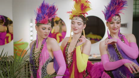 tres damas con vestidos de plumas se divierten y bailan antes del espectáculo