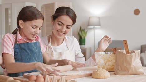 cheerful girl rolling dough for pie with her mommy