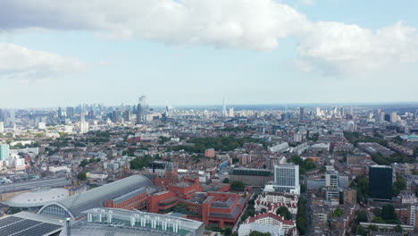 Fly-above-city.-Industrial-or-commercial-buildings-around-St-Pancras-train-station.-Tall-modern-skyscrapers-in-background.-London,-UK