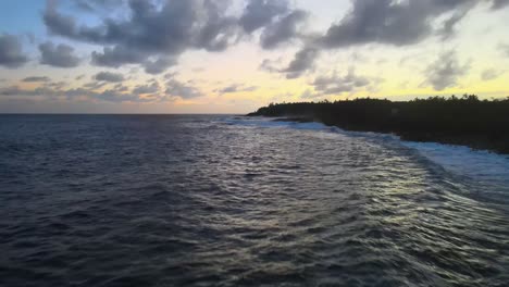 Low-ascend-drone-shot-captures-waves-crashing-on-shore-with-a-sunset-backdrop-on-Big-Island,-Hawaii