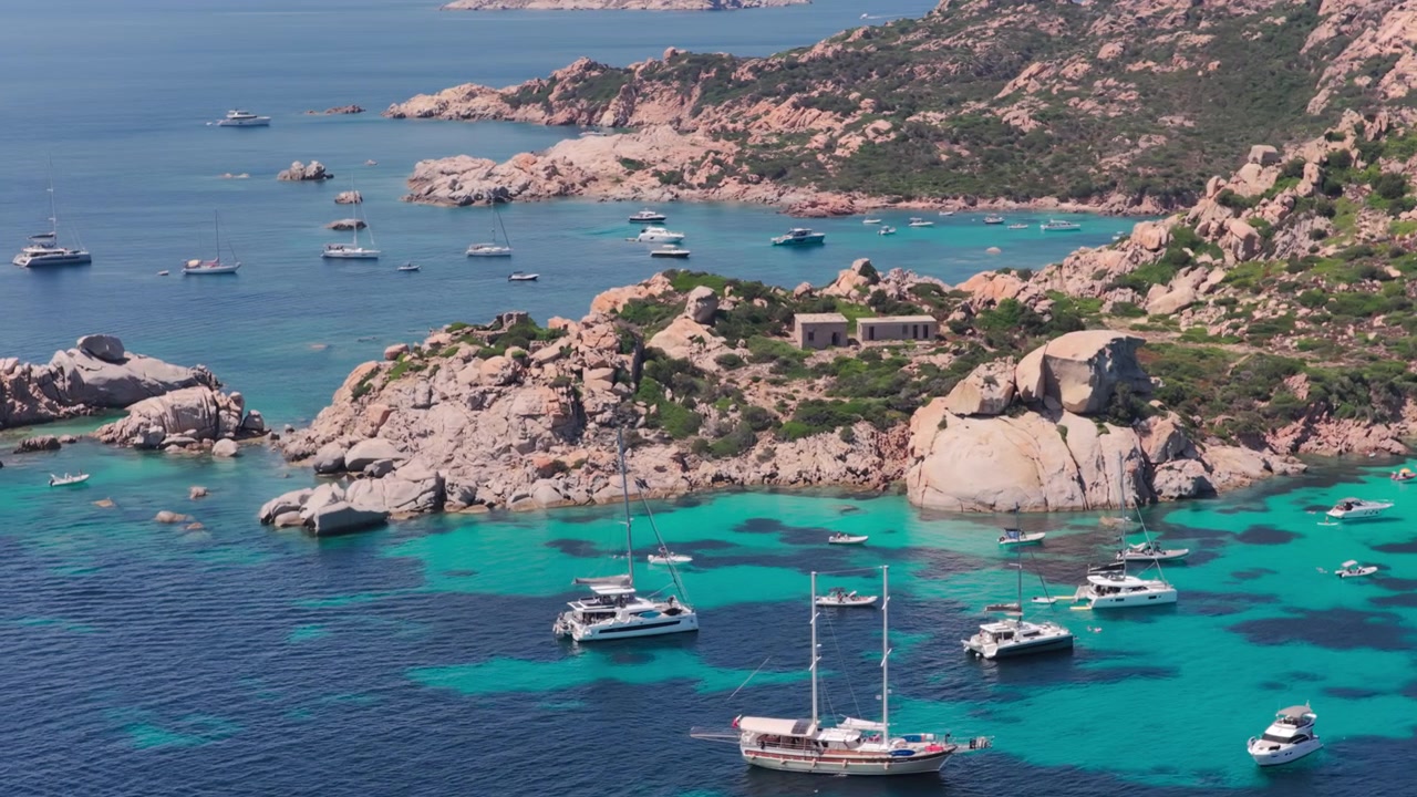 Vue aérienne au téléobjectif de voiliers de luxe et de bateaux de tourisme, révélant une magnifique plage de sable nichée dans des falaises de granit sur l'île de Spargi dans l'archipel de la Maddalena en Sardaigne, Italie