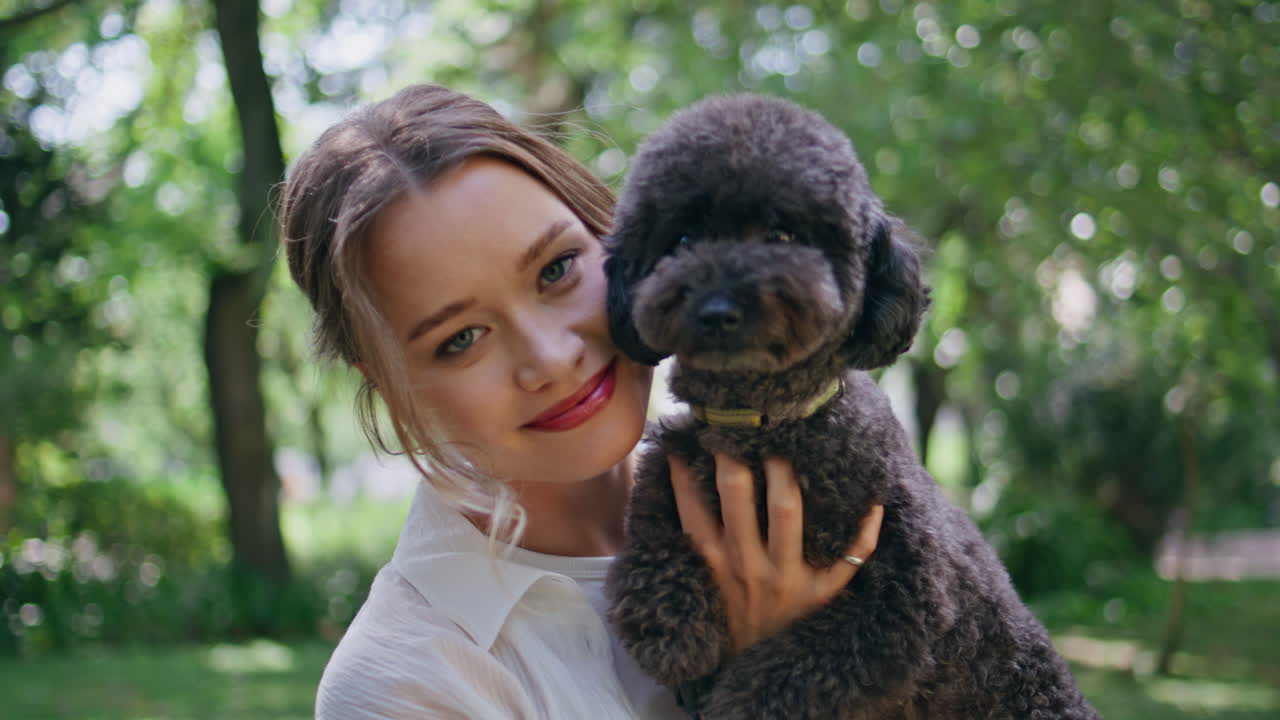 Joyful woman holding puppy on sunny nature closeup. Brunette posing with poodle