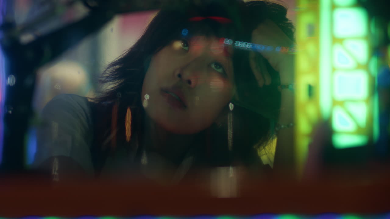 Short haired asian girl plays with hair as she gazes past glass reflecting lights