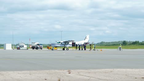 Group-of-professional-skydivers-moving-into-the-white-single-wing-aircraft-before-it-takes-them-up-in-the-sky-for-a-high-altitude-parachute-jump,-sunny-summer-day,-medium-distant-shot