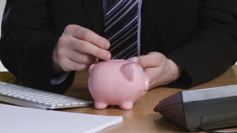 un hombre de negocios poniendo dinero en su alcancía.