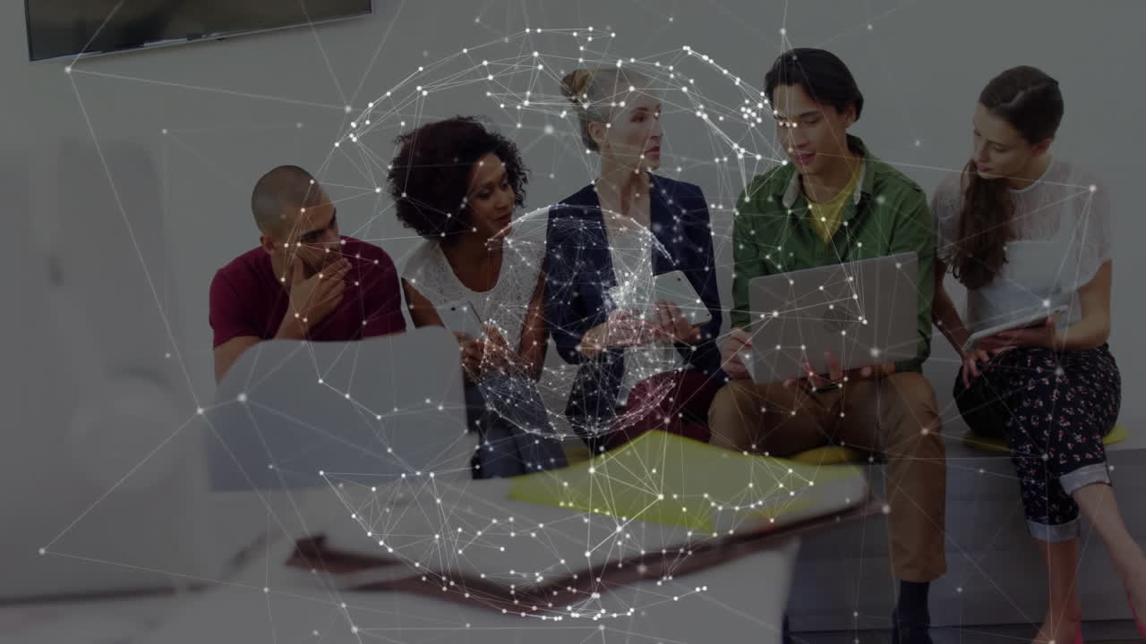 Tech team collaborating over devices in modern office with network overlay hovering above screens