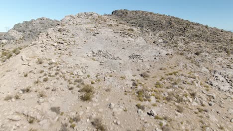 Low-altitude-aerial-climbing-a-moderate-rocky-hill-in-the-Mojave-desert-about-to-reveal-the-vast-emptiness