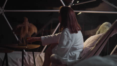 sullen woman relaxes drinking alcoholic drink in glass enjoying night atmosphere on glamping hotel balcony. relaxation in solitude on vacation