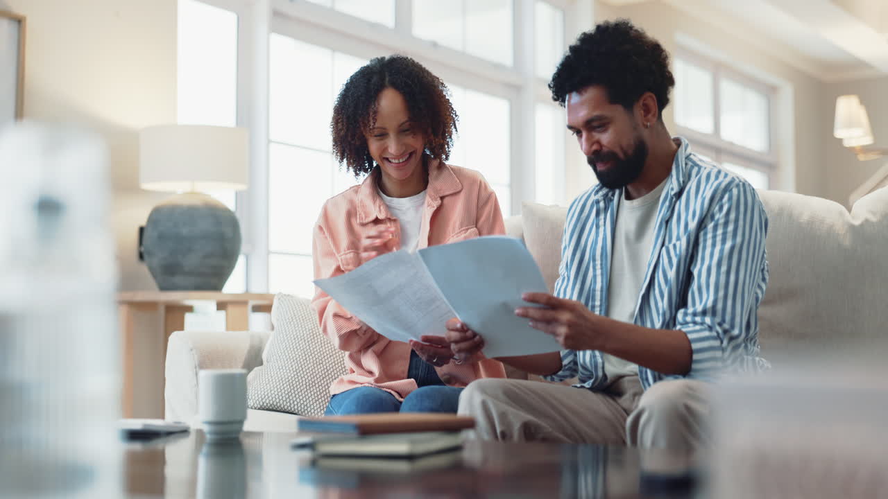 Happy Couple Sitting On Couch Together Reviewing Documents