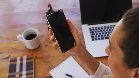 caucasian woman holding smartphone on video call, working from home