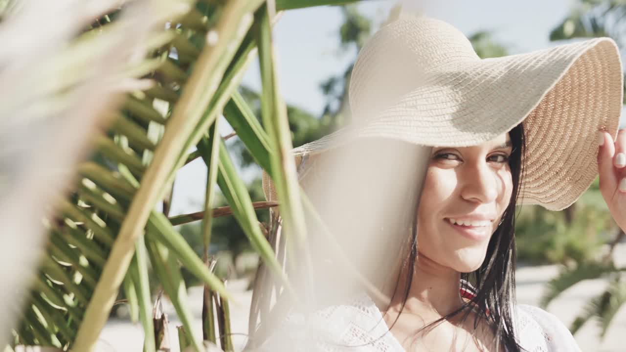 retrato de una feliz mujer hispana con sombrero de sol y vestido de sol sonriendo en una playa soleada, cámara lenta