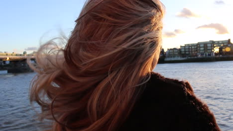 woman's hair blowing around on riverbank at sunset