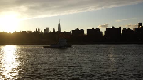 tugboat in hudson river with silhouette of new york city buildings, handheld shot