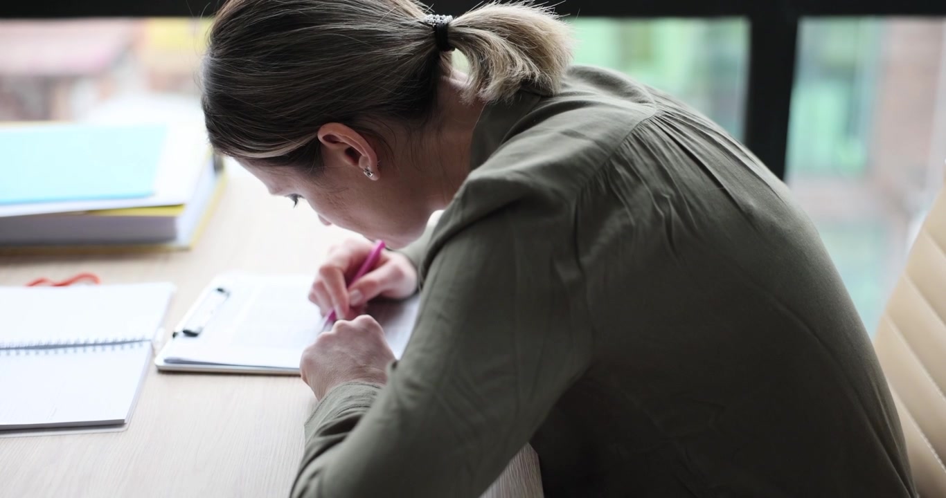 Donna d'affari concentrata prende appunti chinata sulla scrivania in ufficio