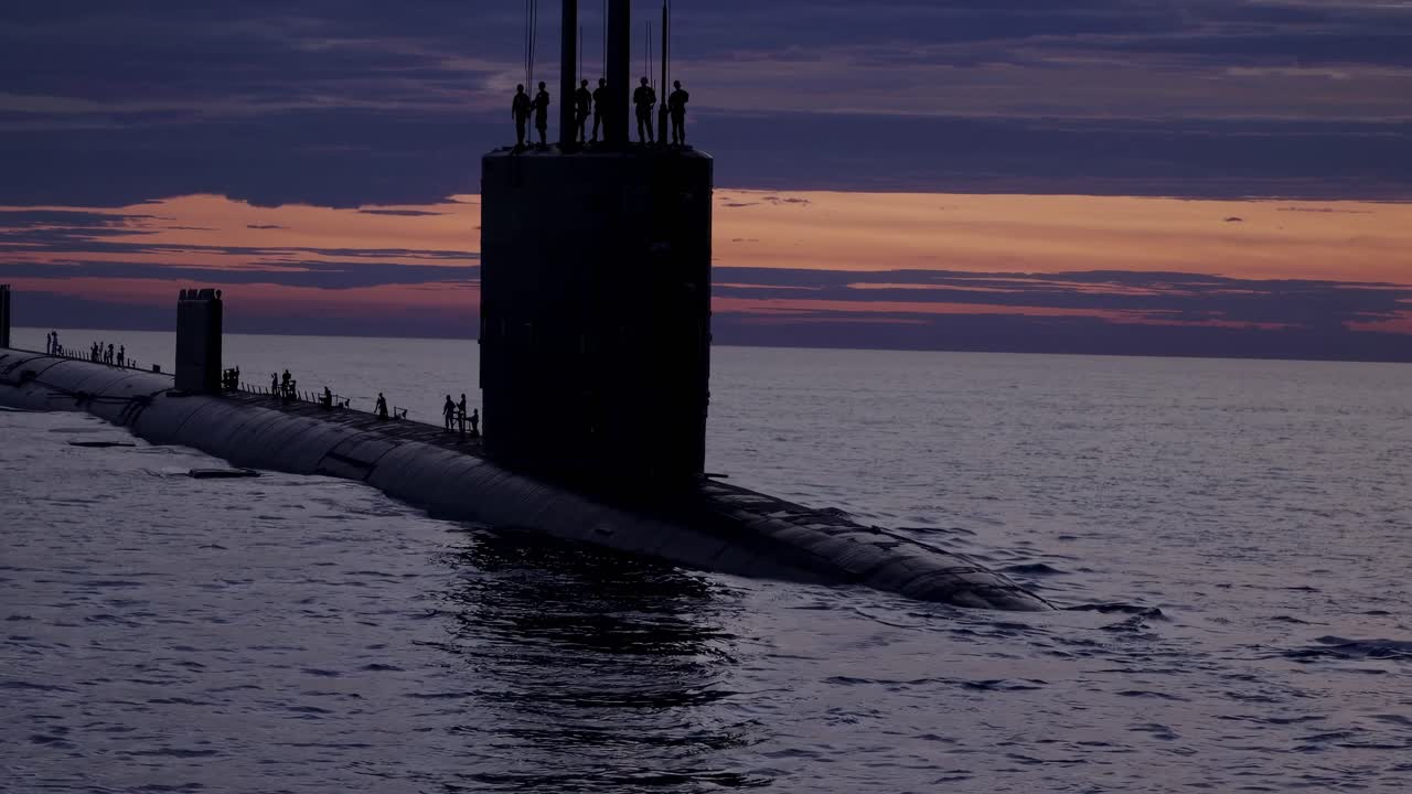 Silhouetted submarine at sunset with crew on deck, captured from a low angle